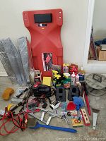 Photo of automotive creeper, jumper cables, small tools, brushes, bottles of cleaning liquids, tire gauges, window screens, and various car maintenance accessories on floor.
