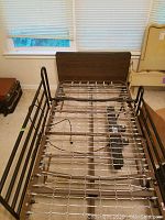 Angle showing the hospital bed metal frame with side rails and wood headboard.