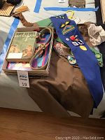 Photo showing Boy Scout book, khaki shirt, blue sash with multiple patches and badges, yellow and red scout neckerchiefs, and part of a belt.