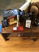 Lot overview showing radios, binoculars, clocks on a small wooden rolling TV stand.
