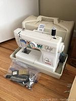 Front view of Elnita Graffiti sewing machine with beige carrying case behind and clear bag of accessories in tray