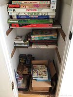 Shelf with stacked vintage board games including Monopoly, Payday, Skip-Bo, Scrabble, My Face, and others with storage boxes below
