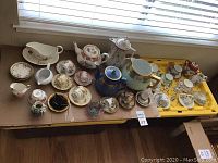 Photo showing 17 cup and saucer sets with floral and gold detailing, along with larger teapots, creamers, and miniature cups arranged on a cardboard surface.