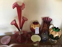 Photo showing the entire lot of six glass decor pieces including blown glass vases with ruffled tops, red stemmed dish, frost yellow candy dish, and ornate gilded vases.