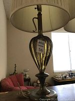 Close-up of one lamp showing fluted green glass base with metal handle and round metal platform base with power cord and tag visible.