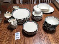 Full set of Pfaltzgraff ceramic dishes including stacks of plates, bowls, cups and saucers displayed on wooden table.