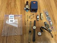 Overview of all 12 watches including boxed Timex watch, metal mesh bands, leather bands, digital and analog faces, and Disney-themed watch in packaging on wooden floor.