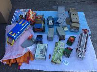 Lot layout showing assortment of vintage metal trucks, Hot Wheels track, model kits, and toy vehicles arranged on a cloth on ground