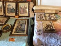 Photo showing multiple framed vintage prints including three hand-colored fashion plates and a Venetian cityscape print on a green towel surface