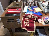 Wide shot of two boxes containing binders and table surface showing pennant and various booklets