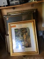 Stacked framed items including one color garden art print and several vintage photographs and empty frames