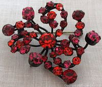 Close-up of vintage Austria signed brooch with prong set fuchsia, red, and deep red rhinestones in black japanned metal setting.