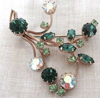 Front of vintage brass brooch with green and AB rhinestones, showing floral or branch-like design