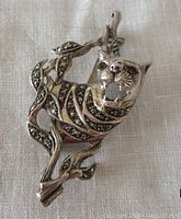 Front view of the sterling silver tiger brooch showing marcasite body and red stone eyes, with detailed open mouth and leaf branch design.