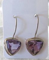 Front view of pair of earrings showing triangular faceted amethyst stones in sterling silver setting attached to curved hooks.