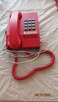 Photo showing a deep red wall mount telephone with coiled handset cord, push button keypad, and intact handset in resting position on the phone base.