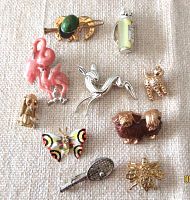Photo showing 10 vintage miniature brooches of various animal, sports, and insect designs arranged on fabric background.