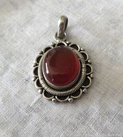 Front view of vintage sterling silver pendant with oval carnelian gemstone set in scalloped and beaded silver frames.