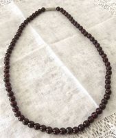 Full view of vintage garnet bead necklace laid on white cloth, showcasing uniform round beads and metal clasp.