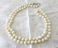 Full length of necklace laid flat on white fabric showing strand doubled and clasp at top