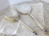 Photo of the vintage Birks sterling silver hand mirror and hair brush set displayed on decorative cloth, showing design and size.