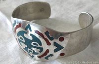 Close-up angle showing front coral and turquoise tribal design on silver bangle