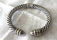 Close up of vintage Milor sterling silver hinged bangle with twisted rope design and two-tone accents, shown flat on light fabric background.