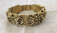 Front view of hinged clamper bangle showing heavily embossed floral lilies design in brass tone