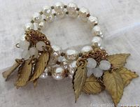 Photo showing two strands of vintage coil bracelet made with baroque imitation pearls, brass leaves, and white bead clusters.