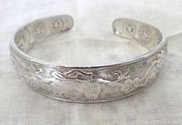 Photo showing front side detail of the floral embossed sterling silver rigid bangle bracelet on a neutral cloth background.