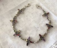 Full view of the silver link bracelet with multi gemstone clusters on a white fabric background.