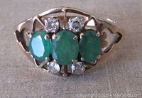 Front view of ring showing three oval emeralds flanked by four round diamonds