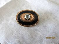 Front view of oval Victorian brooch showing black onyx base, gold filled engraving, and central clear facetted glass stone.