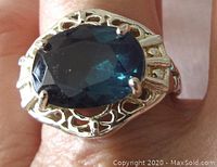 Close-up top view showing the deep blue-green oval faceted stone set in an open work sterling silver setting on finger.