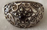 Close-up front view of a vintage sterling silver ring showing detailed openwork with marcasite stones arranged around a central black stone in a floral pattern.