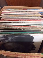Box of over 60 vinyl LP records stacked upright showing mixed condition and genres
