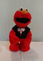 Front view of the bright red Elmo plush with black shirt and 'ELMO' logo.