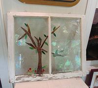 Front view of antique window with stained glass tree and bird design, showing weathered white wooden frame