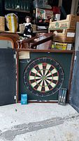 Dartboard in its wooden folding case with darts and chalk accessory, showing setup and size.