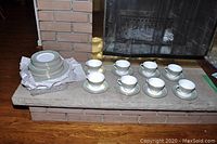 Full lot with cups, saucers and stacked plates displayed on fireplace ledge, showing whole set and included items.
