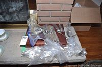 Wide view showing assorted flatware pieces partially wrapped in plastic on a wooden storage case