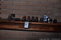 Collection of various figurines placed on a wooden shelf against a brick wall, including shoe figurines, dog figurine, and glass art balls.