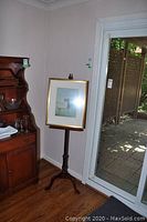 Full view of framed picture on wooden stand in room corner with hardwood floor and sliding door.