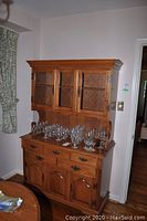 Front view of wood buffet and hutch with glass doors and glassware on top.