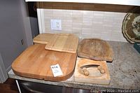 Photo of six wooden cutting boards and one cutting blade on countertop, showing shape and wear.