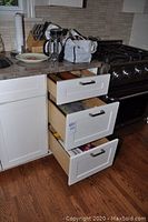 Overall view of kitchen corner with open drawers showing some kitchen tools and supplies on counter and inside drawers.