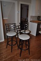 Three black tubular metal bar stools with round white vinyl seats in a kitchen setting