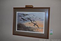 Framed print by artist Maynard Reece depicting geese in flight over marshland with sunset, mounted in brown wooden frame with gold accents and double matting.