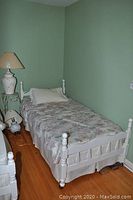 Single bed fully made with floral bedding and white pillow. Shows painted wooden frame with some wear.