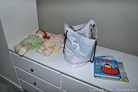 Two Cabbage Patch dolls and a bag containing clothing and four children's books on white dresser
